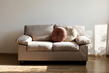 Minimalistic image, beige textile couch with round cushions over the blank wall background with a lot of copy space for text. Empty room interior with just a single sofa. Close up.