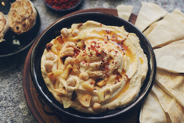 Traditional homemade middle eastern dish - hummus decorated with chickpeas, garlic, olive oil and spices on dark stone table