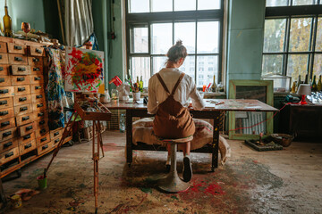 Backview of female artist working at her studio - obrazy, fototapety, plakaty