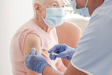 Portrait of elderly woman at the hospital being vaccinated by a female nurse. Senior lady wearing face mask getting an immunization shot. Close up, copy space, background. - obrazy, fototapety, plakaty