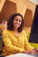 Businesswoman Wearing Phone Headset Talking To Caller In Busy Customer Services Centre