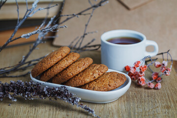Oatmeal cookies with hot tea on a natural wood desk. Winter composition for the interior with snow-covered branches and rowan berries. Horizontal photo in actual shades of brown.