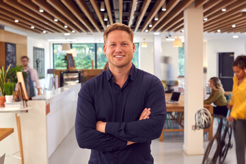 Portrait Of Smiling Businessman Standing In Busy Office Coffee Shop