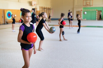 Girl gymnast doing exercise with ball on training in gym with other girls