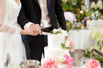 Bride and groom holding knife and cutting stylish white wedding cake with flowers. modern big wedding cake with pink and white roses