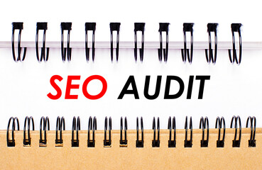 Text SEO AUDIT on white paper between white and brown spiral notepads.