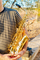 Young man standing holding a saxophone in a natural and sunny place.