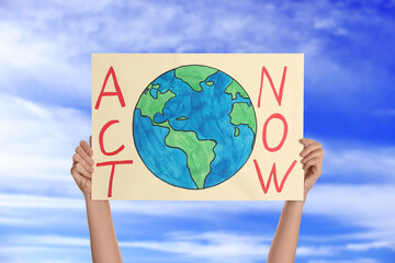 Protestor holding placard with text Act Now against blue sky, closeup. Climate strike