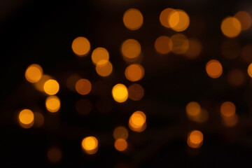 Defocused bokeh lights on black background, an abstract naturally blurred backdrop for Christmas eve or birthday party. Festive light texture. Yellow and red garland in blur. Overlay effect for design