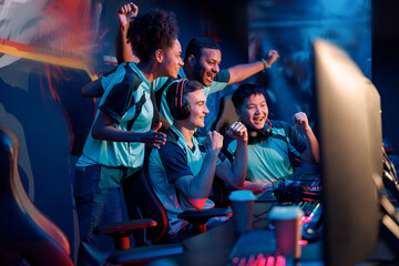 Fototapeta na wymiar Multiracial cybersport gamers expressing success while raising hands up and smiling during participation in esports tournament in computer club