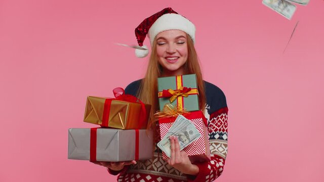 Adult girl in Christmas sweater holding gift boxes. Concept of spending money, shopping online. Money cash dollars falling. Black Friday. Good holiday low prices. Pink background. Happy New Year sale