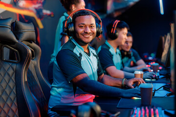 Professional cybersport gamer looking at camera and smiling while using powerful computer for online game in computer club © Yaroslav Astakhov