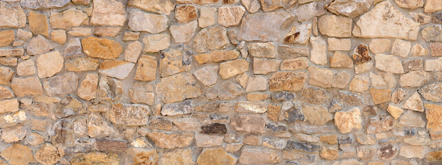 Grobe Wand aus verschiedenen hellbraunen Natursteinen in Panorama Nahaufnahme