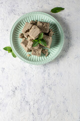 Pieces of halva on green plate. Sweet dessert with mint leaves on white background