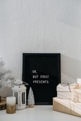 Many craft Christmas gift boxes and black letter board with quote Ok but first presents. Festive Christmas letter board ideas and quotes. Blackboard with the Xmas phrase on table