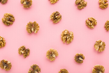 Obraz na płótnie Canvas Brown walnuts on light pink table background. Pastel color. Closeup. Food pattern. Top down view.
