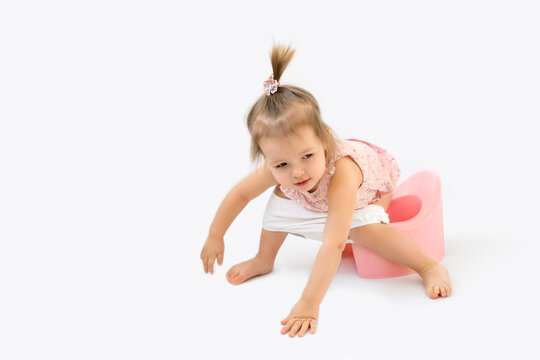 A small one-year-old baby sits on a pot with her panties down. Teaching a child to go pee on a potty. Toddler on a white studio background. 