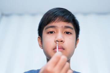 Asian boy self collecting nose swab for corona virus sample.Covid-19 laboratory test.Antigen test kit for rapid nose swab.Nasal swab is a test that takes a sample of cells from the nasopharynx.