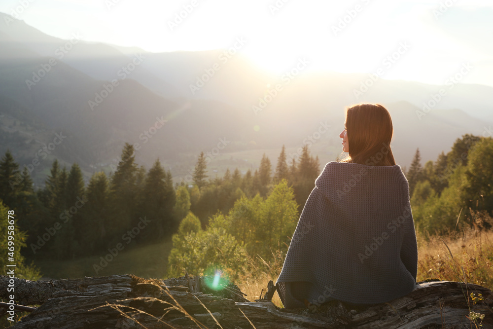 Wall mural Woman with cozy plaid enjoying sunset in mountains, back view