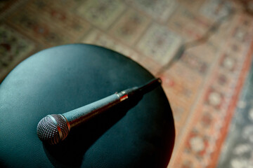 A wired scuffed microphone lies on a chair stool on stage with a vintage carpet in front of the...
