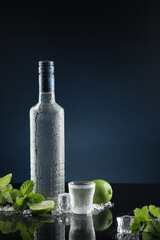 Ice-cold bottle of vodka with shot glasses on dark blue background with copy space. Vertical format. - obrazy, fototapety, plakaty