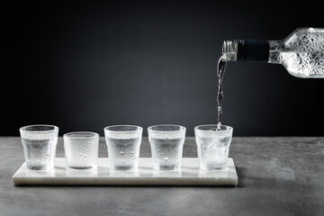 Pouring cold vodka into shot glass isolated on dark background. Selective focus. - obrazy, fototapety, plakaty