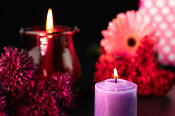 Obraz na płótnie Canvas Flames Glowing From Designer Purple Or Lilac Pillar Candle With Colorful Fresh Floral Theme On Dark Black Background