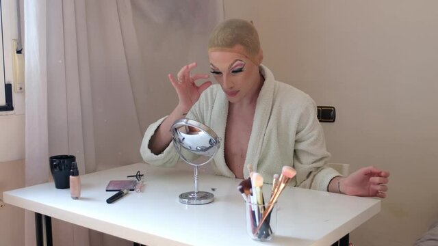Drag queen person removing false eyelashes and wearing bathrobe.