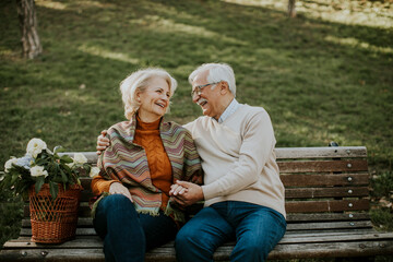 Fototapeta premium Senior couple sitting on the benchwith basket full of flowers and embracing