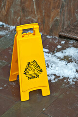 Yellow danger sign. Symbol of a slippery sidewalk. Inscription attention in different languages. Plate near the cobblestones in the spring.