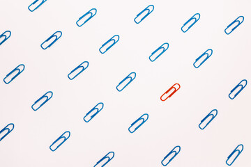 A red paper clip stands out against a background of blue paper clips.