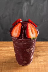Brazilian Frozen Açai Berry Ice Cream Smoothie in plastic cup with Strawberries. On a wooden desk...