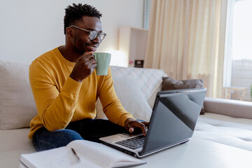 Photo series of African-American businessman at his home office taking a coffee break, while working on computer. Shot of handsome young black man happily working on his laptop at home during the day.