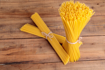 A vertical bunch and a bunch of raw spaghetti tied with string. Bundle on a wooden background.