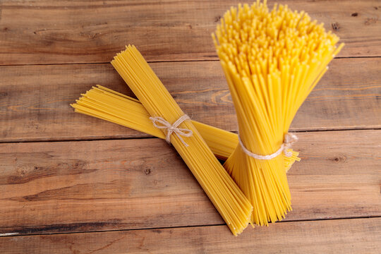 A Vertical Bunch And A Bunch Of Raw Spaghetti Tied With String. Bundle On A Wooden Background.