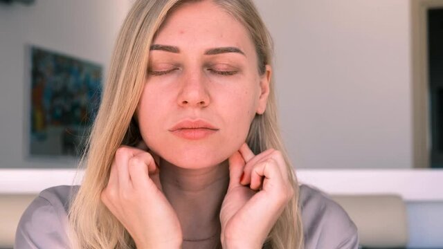 Facebuilding. Double chin problem. Portrait of a young attractive blonde woman doing a facial massage with her fingers. Self-care. Combating age-related changes. 4k, slow motion