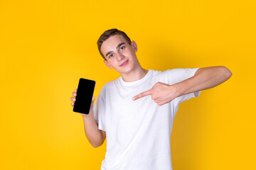 A handsome guy in a white t-shirt  showing smartphone on a yellow background