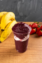 Brazilian Frozen Açai Berry Ice Cream Smoothie in plastic cup with Condensed Milk. On a wooden...