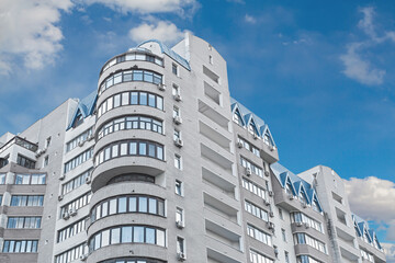 Facade of a high-rise apartment building against a blue sky with fluffy cumulus clouds