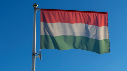 National flag of Hungarian on a flagpole in front of blue sky with sun rays and lens flare. Diplomacy concept.