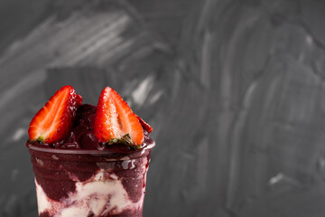 Brazilian Frozen Açai Berry Ice Cream Smoothie in plastic cup with Straw Berries and Condensed Milk. On a wooden desk and a gray summer background. Front view for menu and social media
