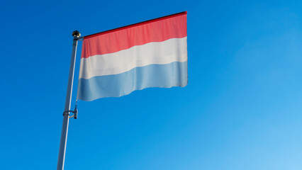 National flag of Luxembourg on a flagpole in front of blue sky with sun rays and lens flare. Diplomacy concept.