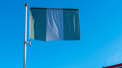 National flag of Nigeria on a flagpole in front of blue sky with sun rays and lens flare. Diplomacy concept.