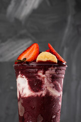 Brazilian Frozen Açai Berry Ice Cream Smoothie in plastic cup with Strawberries, Bananas and Condensed Milk. On summer gray background. Front view for menu and social media