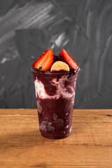 Brazilian Frozen Açai Berry Ice Cream Smoothie in plastic cup with Strawberries, Bananas and Condensed Milk. On summer gray background. Front view for menu and social media