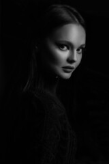 Black and white portrait of a beautiful brunette girl in a black sweater isolated on a black background.