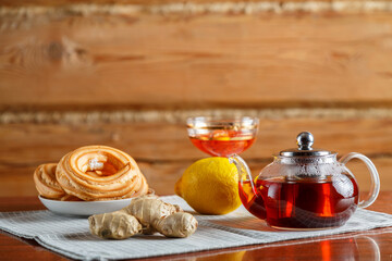A kettle of strong hot tea on the table on a napkin next to lemon, ginger and jam.