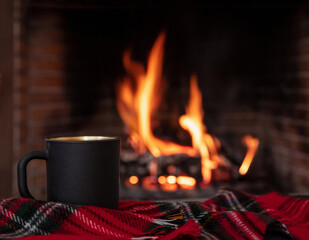 Christmas holiday cozy warm home. Cup of coffee on a sofa blanket, burning fireplace background.