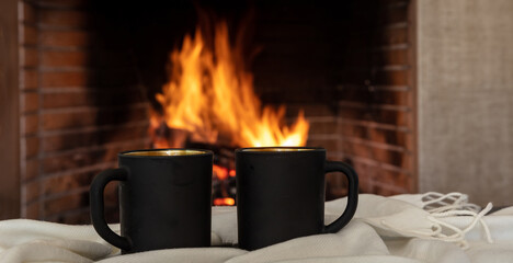 Christmas holiday cozy warm home. Cups of coffee on a sofa blanket, burning fireplace background.