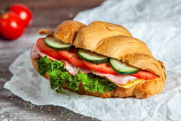 Breakfast of Fresh croissant with ham, cheese and salad leaf on white wooden background.